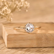 A diamond engagement ring with a large central diamond and smaller diamonds around the edges is displayed on a wooden surface.