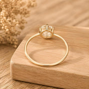 A gold ring with a large diamond set in the center is displayed on a wooden surface, with a blurred floral background.