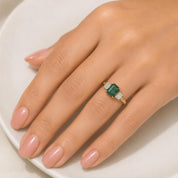 A close-up of a person's hand wearing a gold ring with a green gemstone.