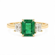 A gold ring with a large, vibrant green emerald gemstone in the center, surrounded by smaller diamonds.