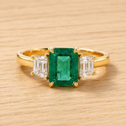 A gold ring with a large, vibrant green emerald gemstone in the center, surrounded by smaller diamonds.