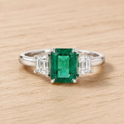 A diamond engagement ring with a large, vibrant green gemstone in the center, surrounded by smaller diamonds.
