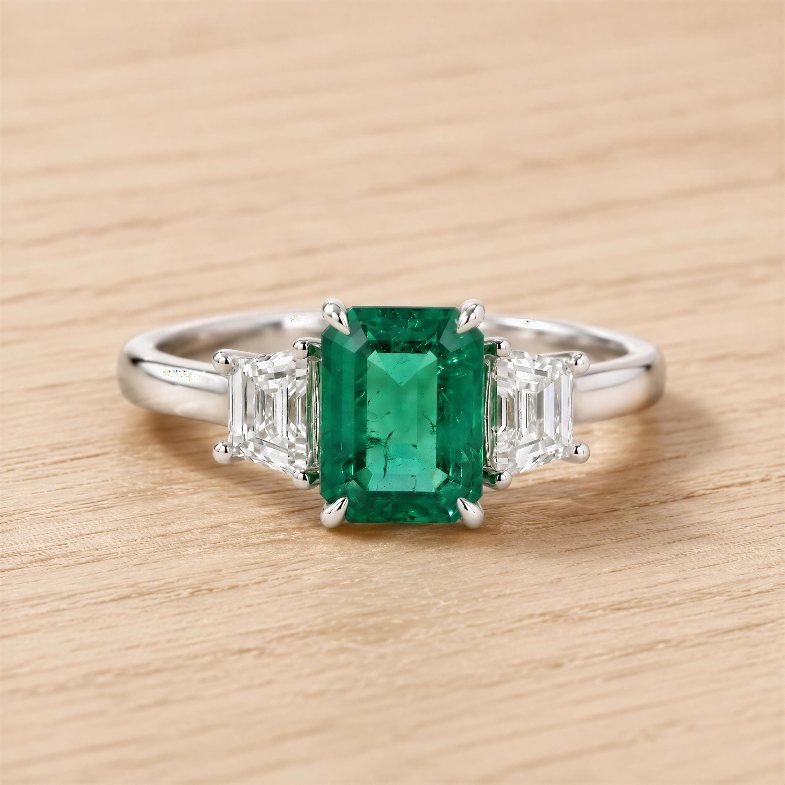 A diamond engagement ring with a large, vibrant green gemstone in the center, surrounded by smaller diamonds.