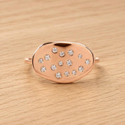 A rose gold ring with a large oval-shaped stone in the center, surrounded by smaller diamonds.