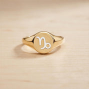 A gold ring with a round embossed sign of the zodiac symbol, which appears to be a Libra sign.