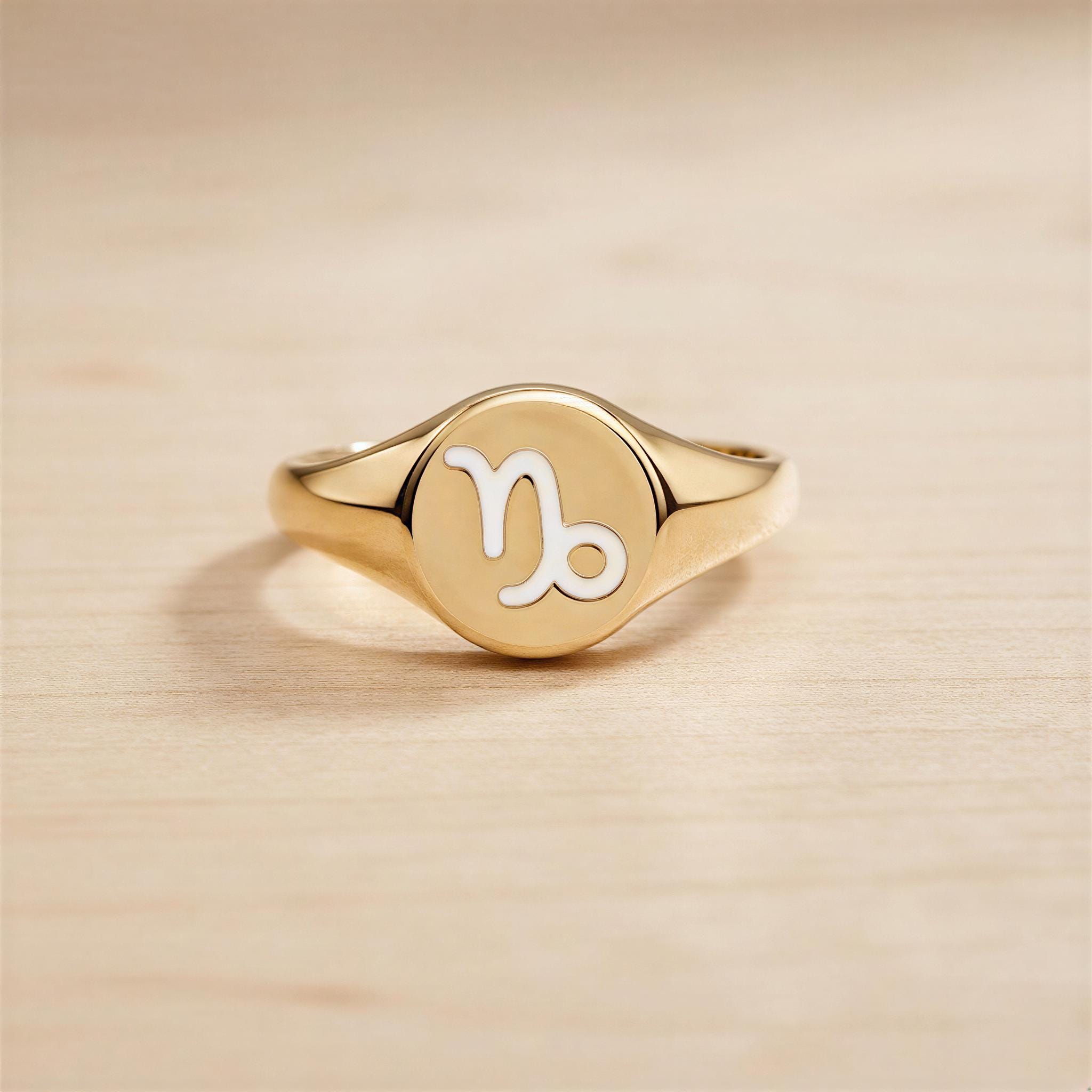 A gold ring with a round embossed sign of the zodiac symbol, which appears to be a Libra sign.