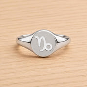 A silver ring with a round, engraved charm featuring the astrological sign of Capricorn.