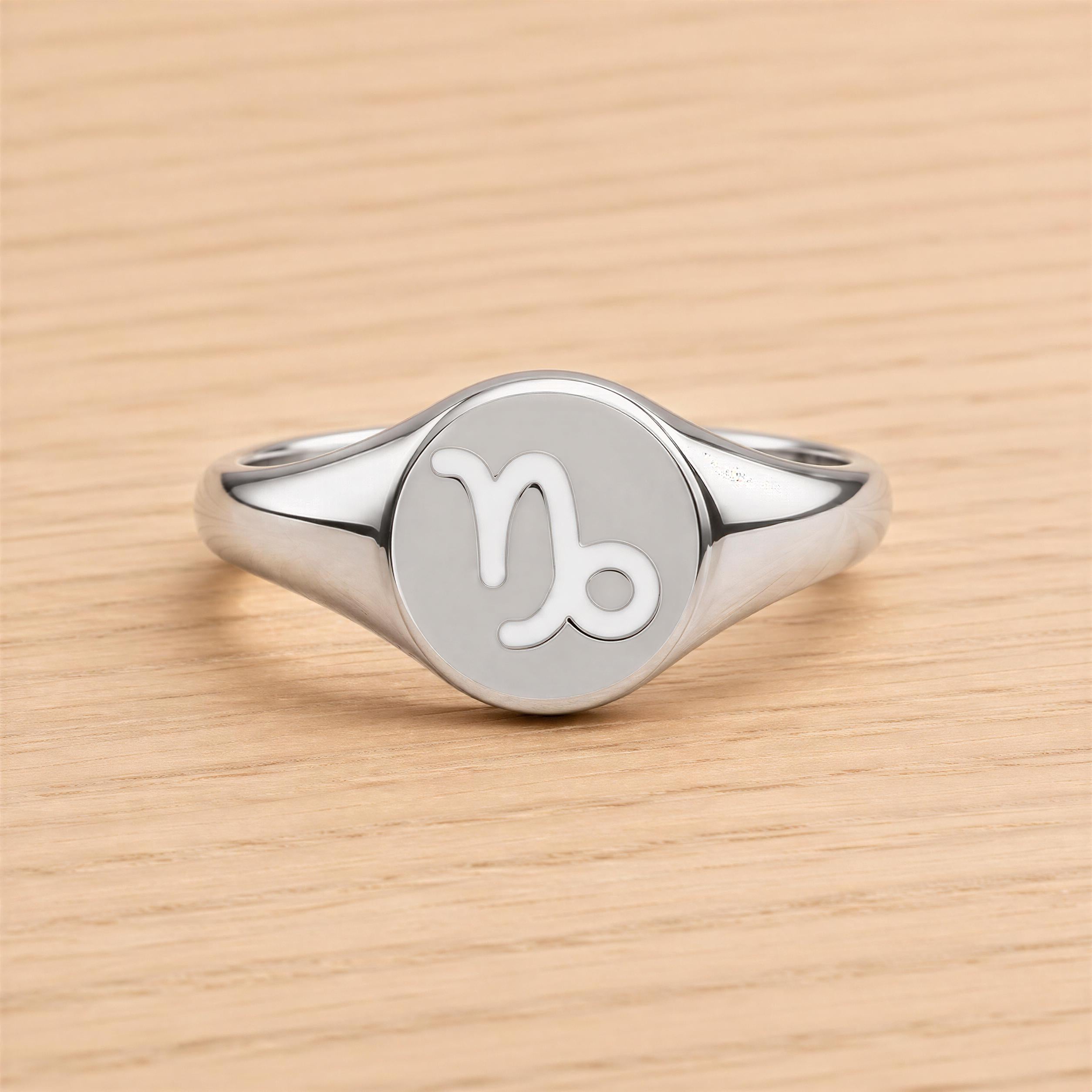 A silver ring with a round, engraved charm featuring the astrological sign of Capricorn.