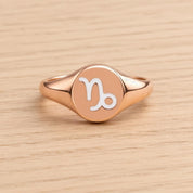 A rose gold ring with a round, engraved signet style ring featuring the astrological sign of Capricorn.
