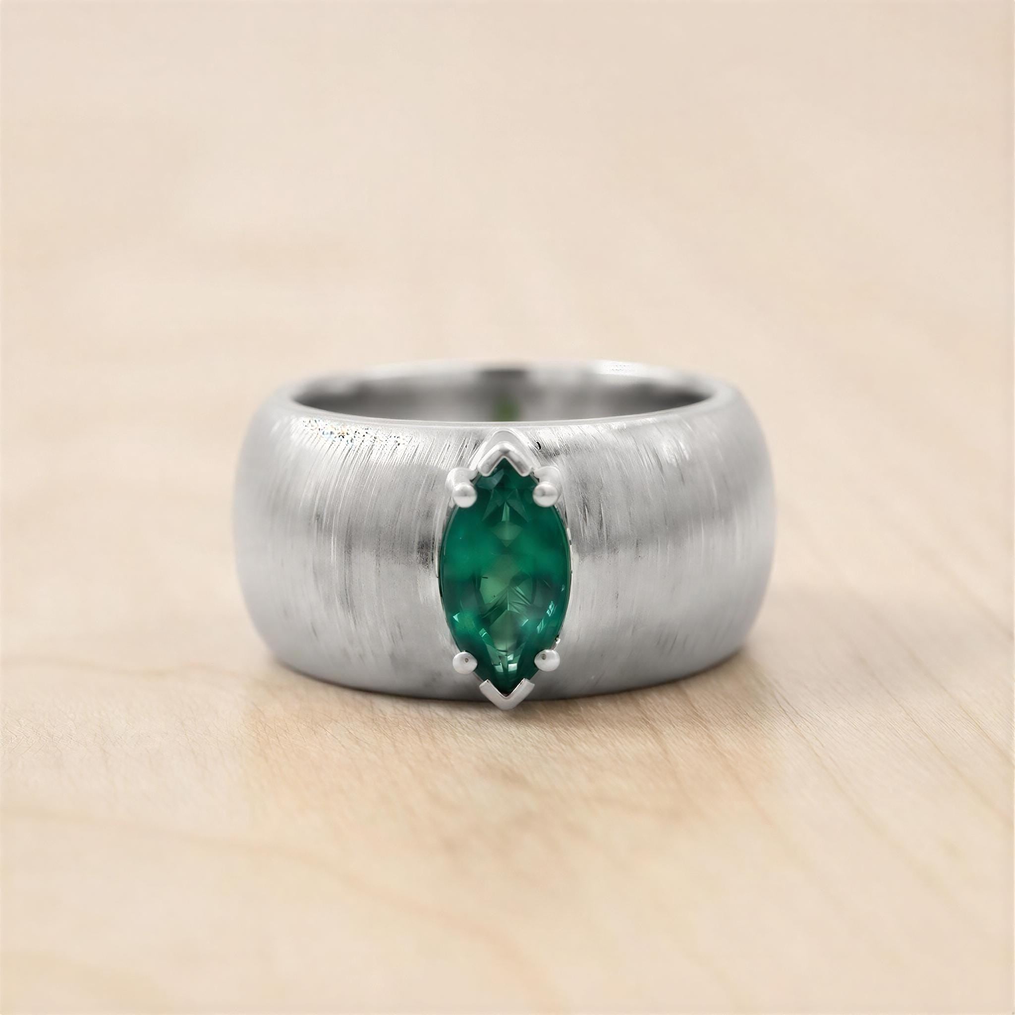 A silver ring with a large green gemstone, possibly a sapphire, set in the center.