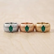 Three rings with a green gemstone are displayed on a wooden surface.