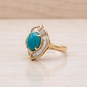 A gold ring with a turquoise gemstone, possibly a pearl, set in a decorative design.