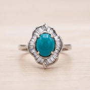 A silver ring with a large turquoise gemstone at the center, surrounded by smaller diamonds.