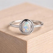 A silver ring with a large oval-shaped opal stone set in the center, surrounded by smaller diamonds.