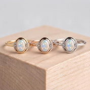 Three rings with opals are displayed on a wooden surface.