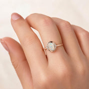 A close-up of a person's hand wearing a gold ring with an oval-shaped opal stone.