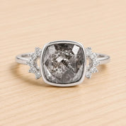A silver ring with a large, irregularly shaped gray gemstone in the center, surrounded by smaller diamonds on either side.