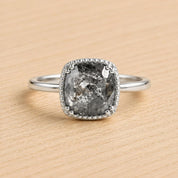 A silver ring with a large, irregularly shaped diamond as the centerpiece, set in a halo of smaller diamonds.