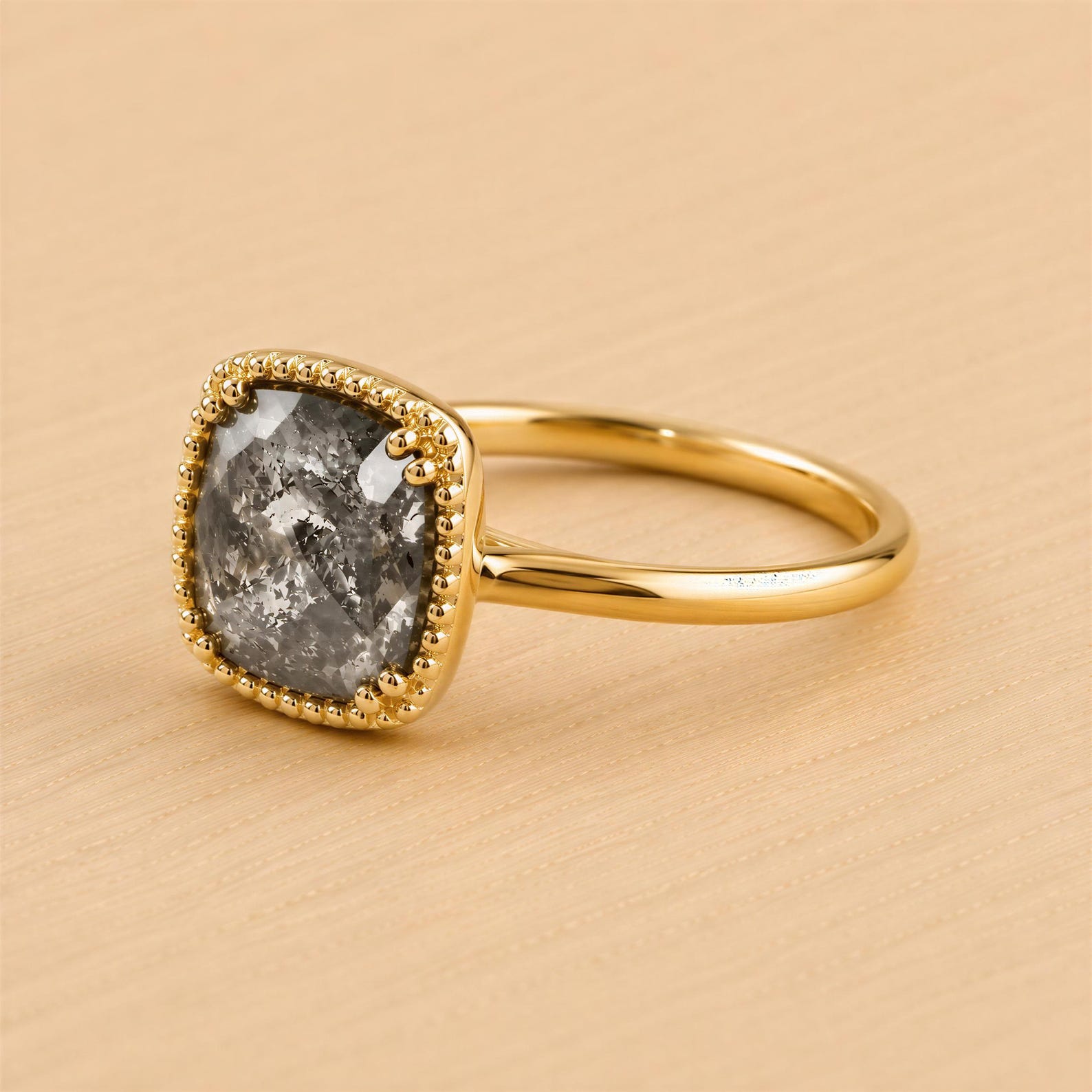 A gold ring with a large, square-shaped gray stone set in the center, surrounded by a decorative gold border.