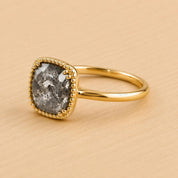 A gold ring with a large, square-shaped gray stone set in the center, surrounded by a decorative gold border.
