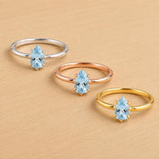 Three rings with blue gemstones are displayed on a wooden surface.