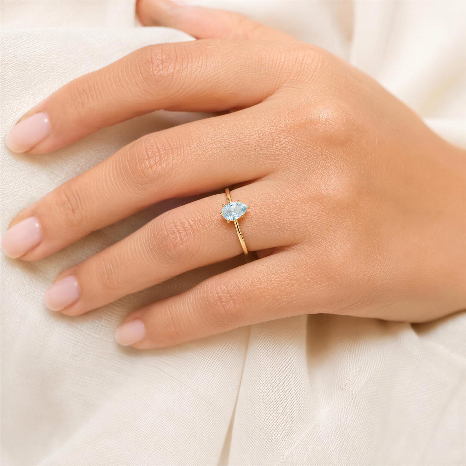 A close-up of a hand wearing a gold ring with a blue gemstone.