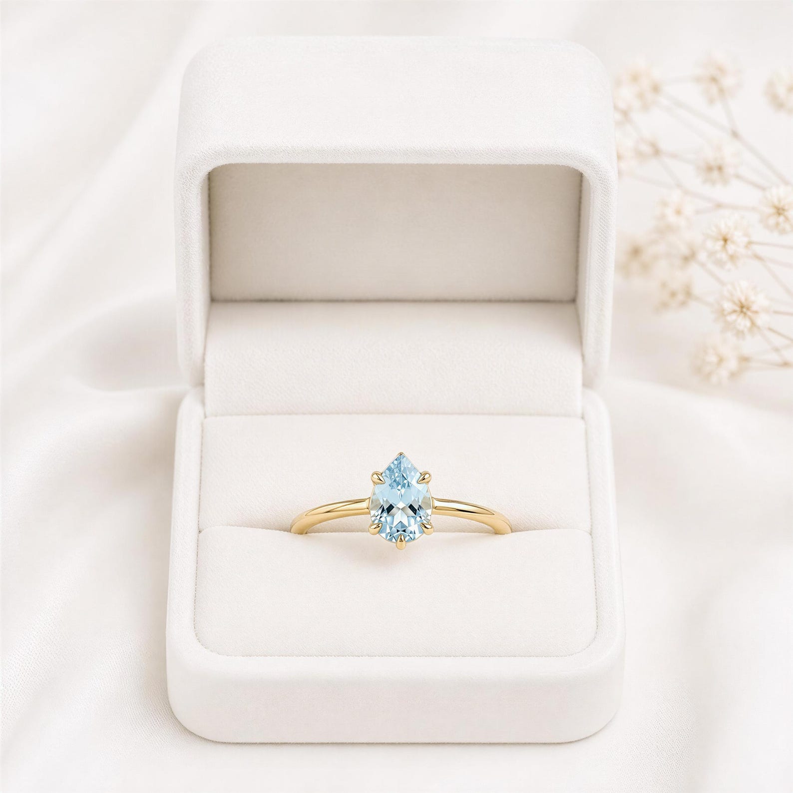 A gold ring with a blue gemstone is displayed in a white jewelry box on a white background.
