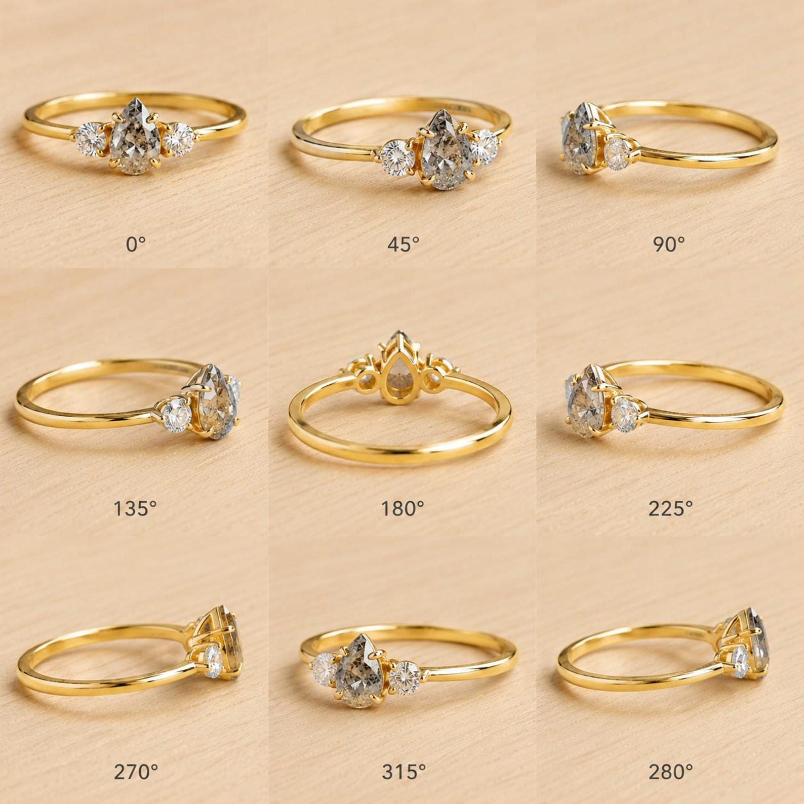 May include: A gold ring featuring a central pear-shaped salt and pepper diamond flanked by two smaller round brilliant-cut diamonds. The image displays the ring from nine different angles labeled from 0 to 315 degrees, showcasing the band and setting.