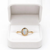 A gold ring with a large oval-shaped opal stone set in the center, displayed in a white jewelry box.