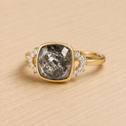 A gold ring with a large gray diamond as the centerpiece, surrounded by smaller diamonds.