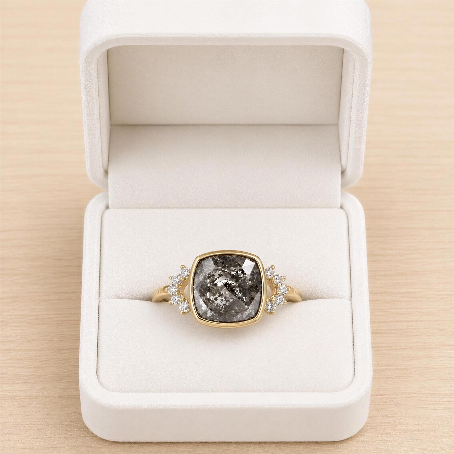 A white jewelry box containing a gold ring with a large gray gemstone, possibly a diamond, and smaller diamonds set in the band.