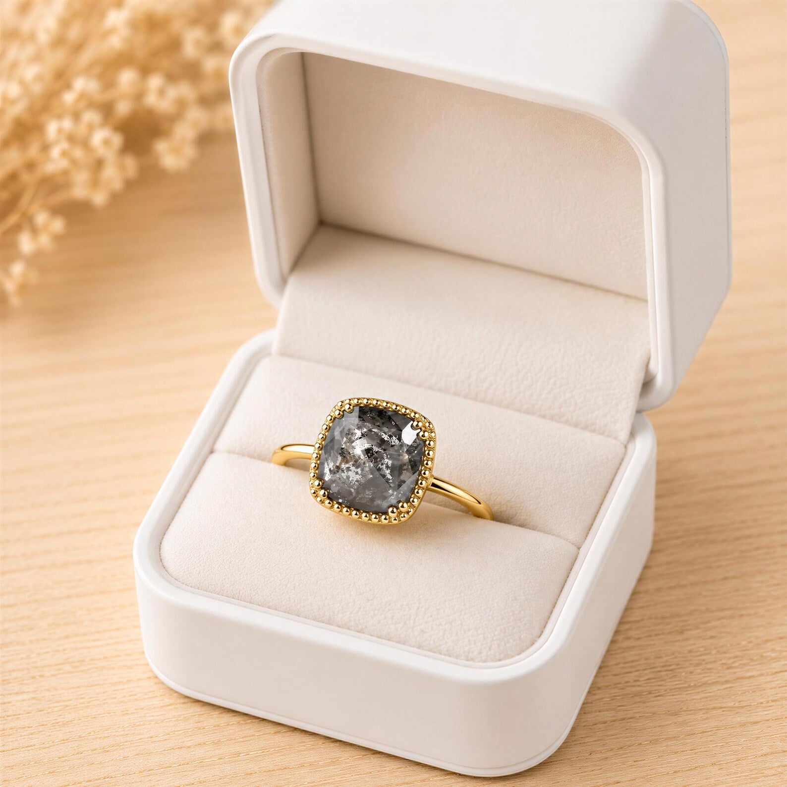 A white jewelry box containing a gold ring with a large, irregularly shaped stone in the center.