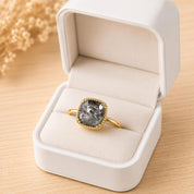 A white jewelry box containing a gold ring with a large, irregularly shaped stone in the center.