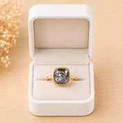 A white jewelry box containing a gold ring with a large, gray gemstone in the center.