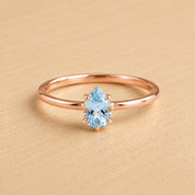 A rose gold ring with a blue aquamarine gemstone set in the center.