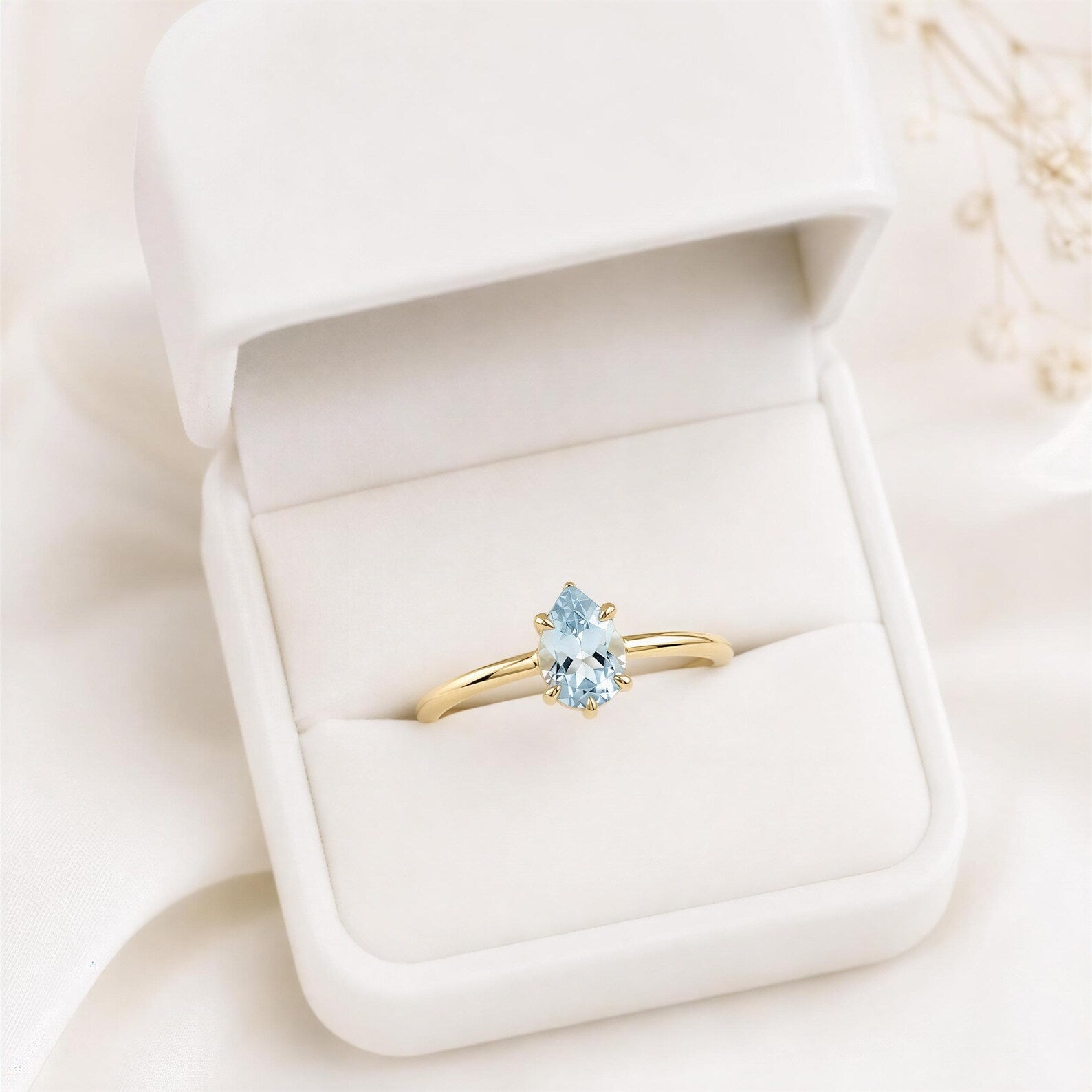 A gold ring with a blue gemstone, placed in a white jewelry box.
