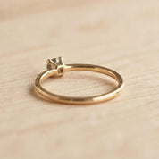 A gold ring with a small diamond set in the center, resting on a wooden surface.