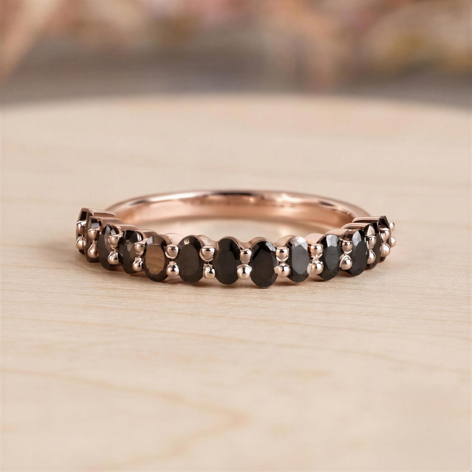 A rose gold ring with a row of black diamonds set in it, resting on a wooden surface.