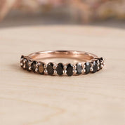 A rose gold ring with a row of black diamonds set in it, resting on a wooden surface.
