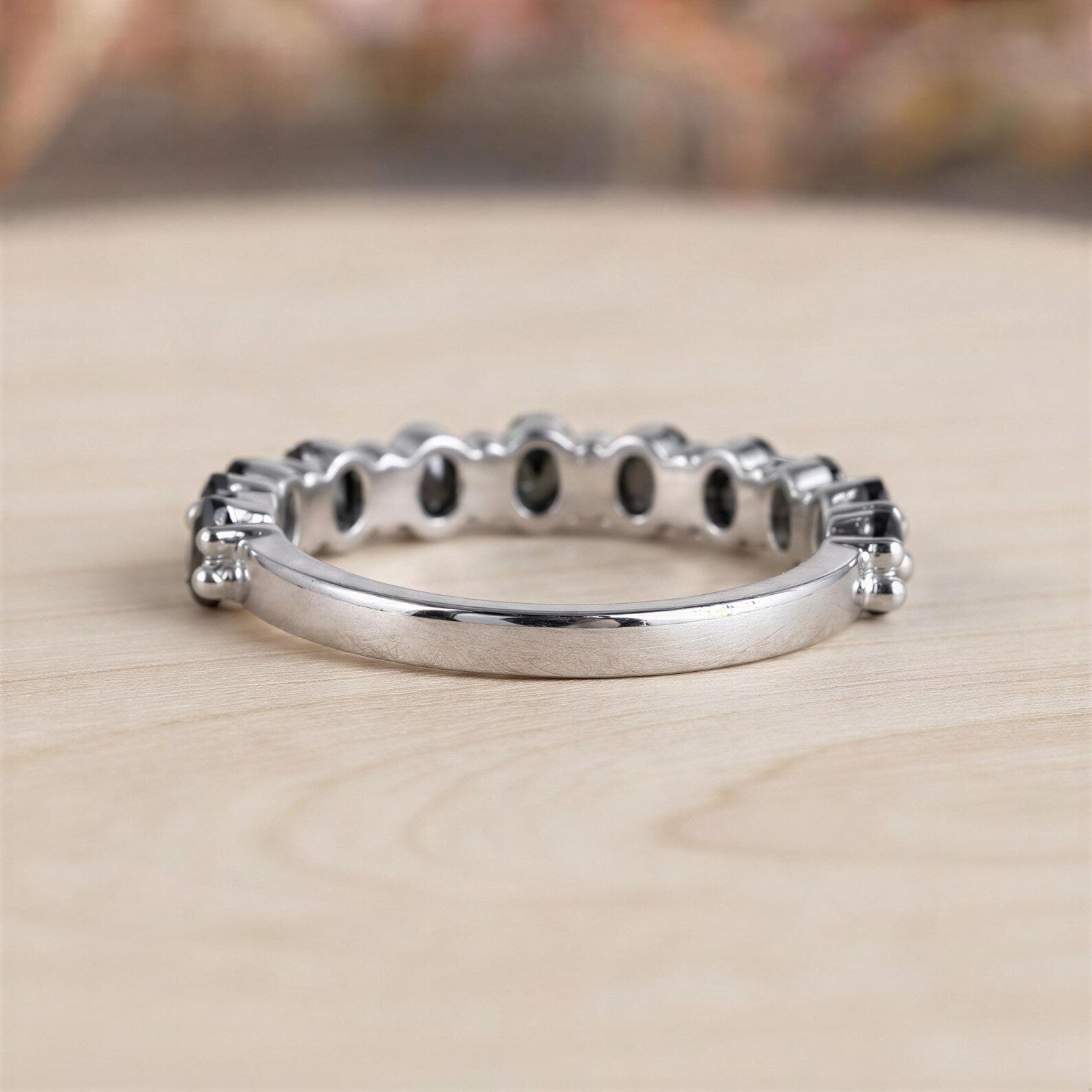 A silver ring with a row of small diamonds or stones set in the band, resting on a wooden surface.