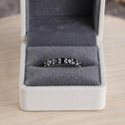 A silver ring with black stones is displayed in a white jewelry box on a wooden surface.
