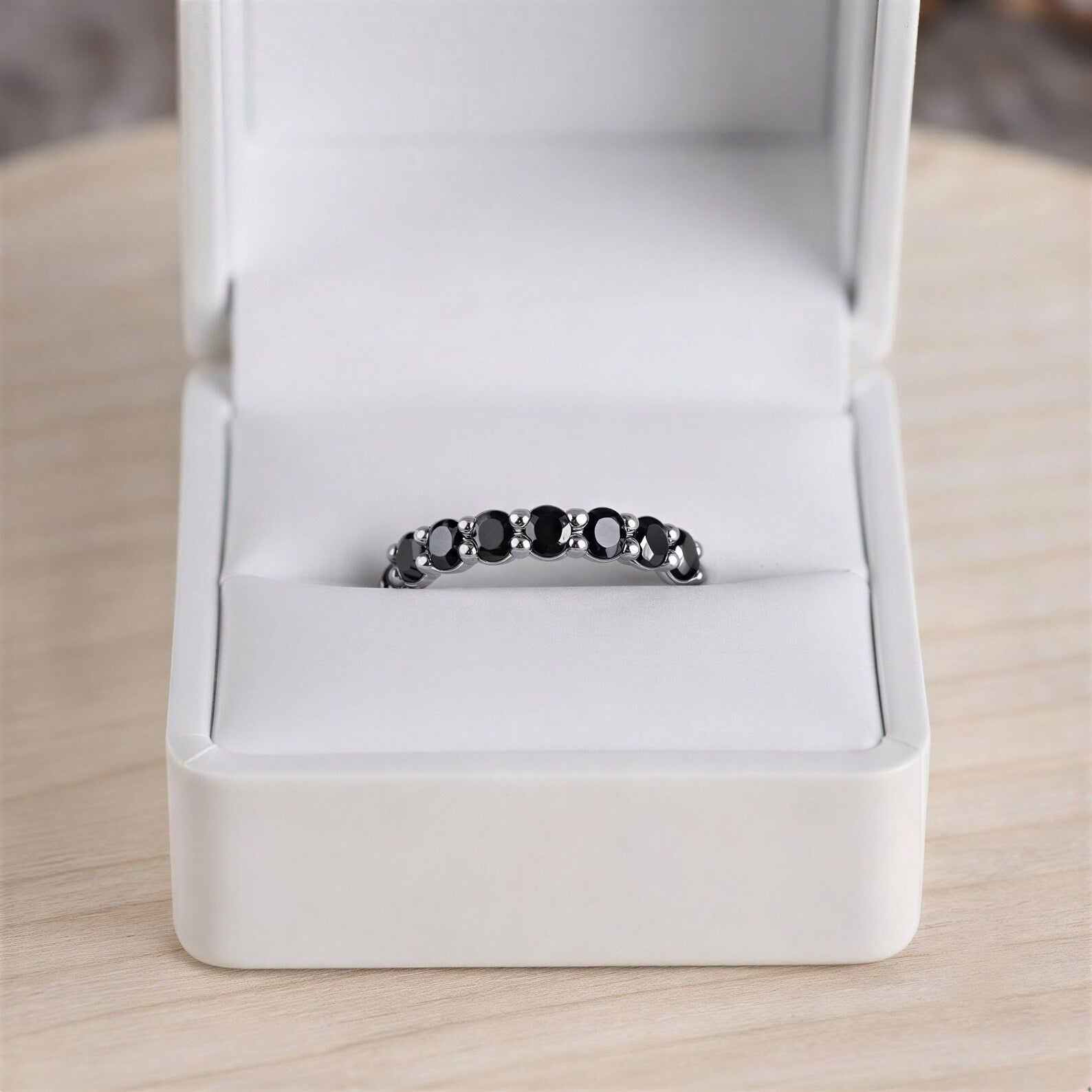 A white jewelry box containing a black and white ring with a row of black gemstones.