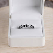 A white jewelry box containing a black and white ring with a row of black gemstones.