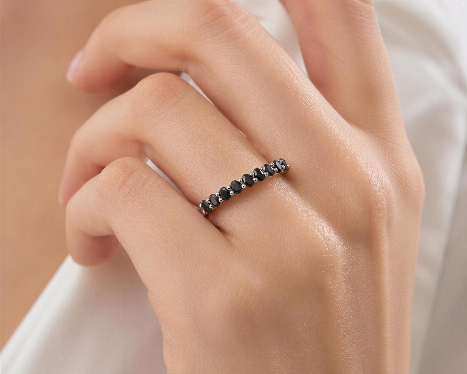 A close-up of a person's hand wearing a ring with a row of black diamonds.