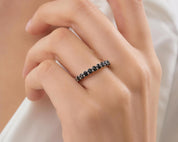 A close-up of a person's hand wearing a ring with a row of black diamonds.