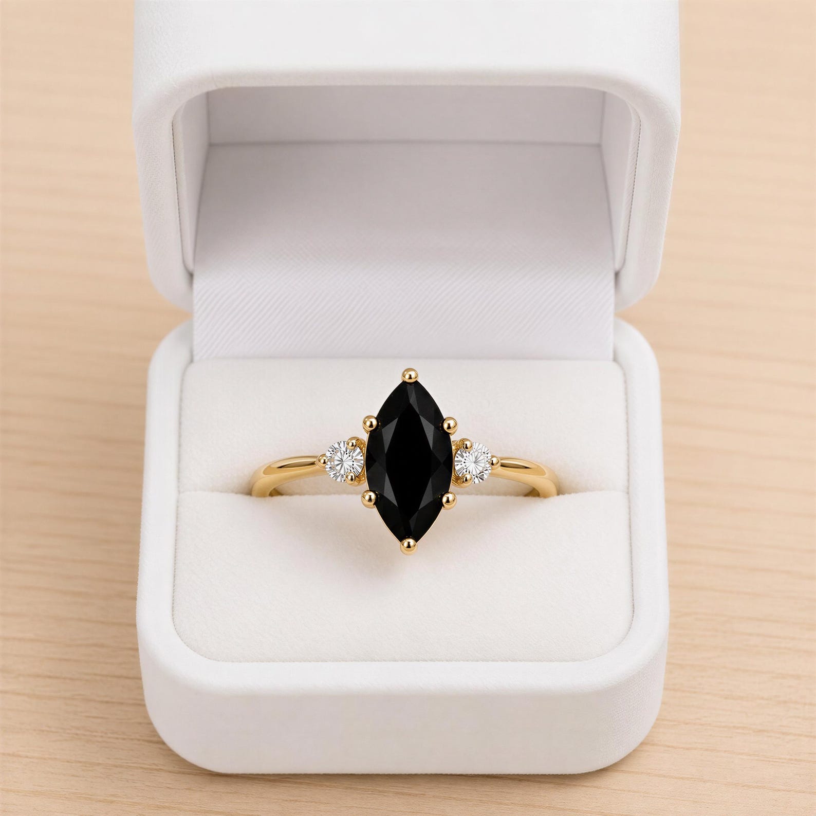 A gold ring with a large black gemstone, possibly a diamond, is displayed in a white jewelry box.