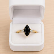A gold ring with a large black gemstone, possibly a diamond, is displayed in a white jewelry box.