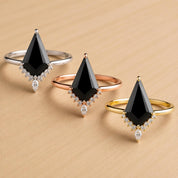 Three rings with black gemstones and gold or silver bands are displayed on a wooden surface.