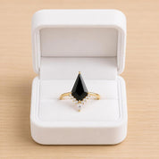 A white jewelry box containing a gold ring with a large black gemstone and smaller diamonds.
