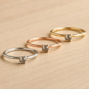 Three rings with a diamond center stone are displayed on a wooden surface.